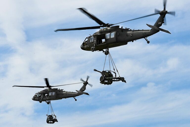 Two black hawk helicopters flying and carrying wepaons.