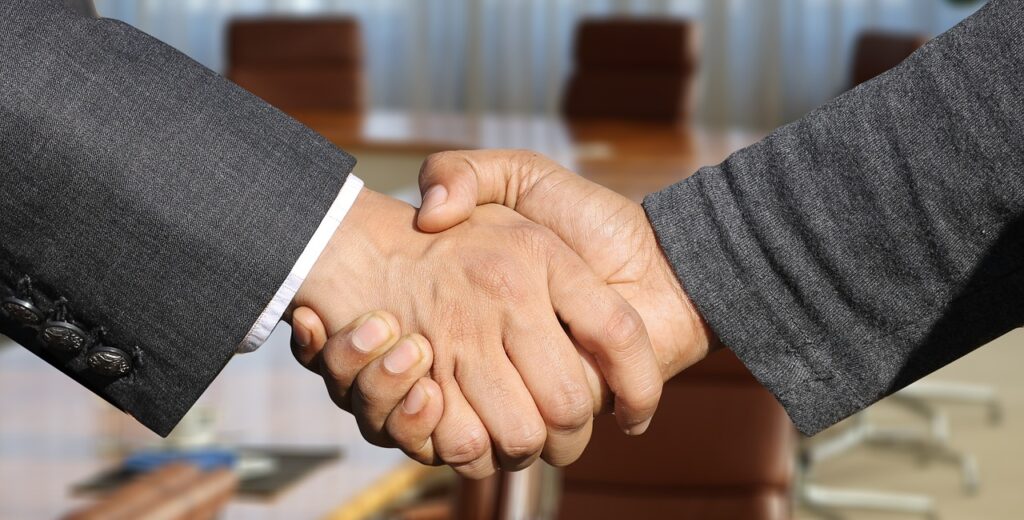 Vet third parties, two businessmen shaking hands over a boardroom table.